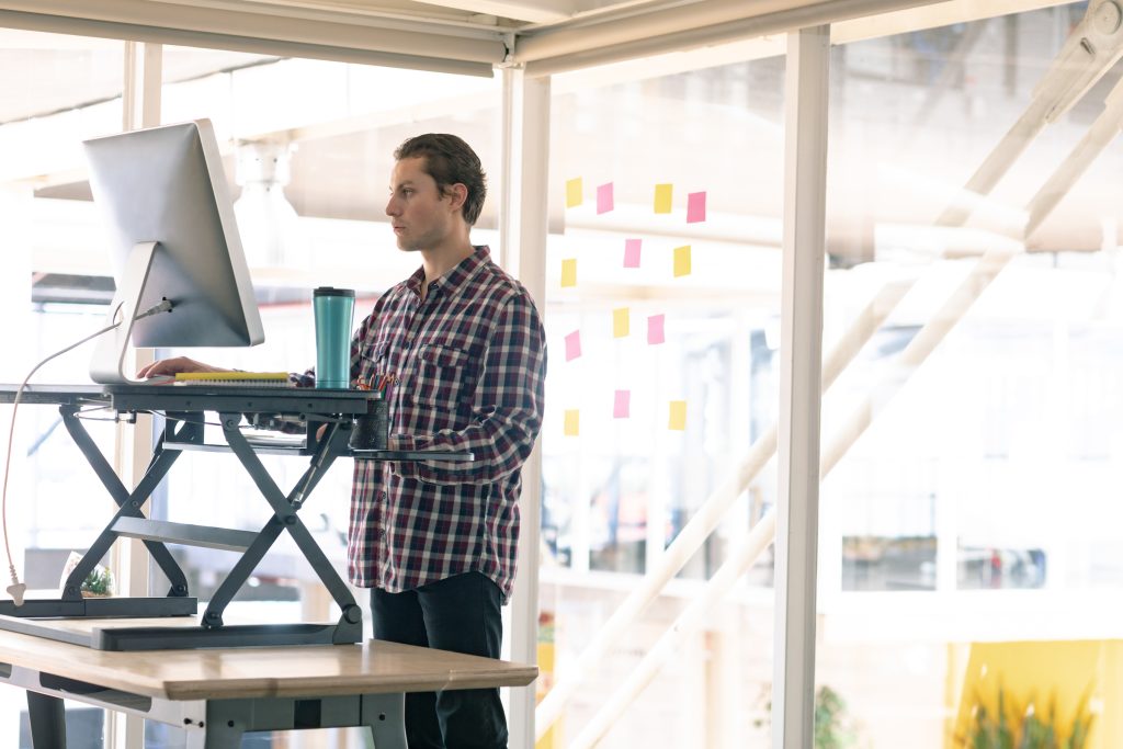 Side view of a person working on computer at standing desk in office